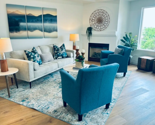 IMG_7890-2 Living room with a cream sofa, teal accent chairs, layered rug, lamps and mountain artwork beside a fireplace.