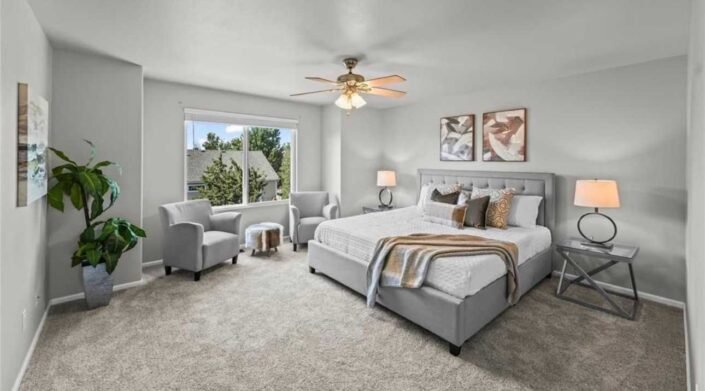 Staged bedroom with a gray upholstered bed, two accent chairs, matching bedside lamps and framed artwork.