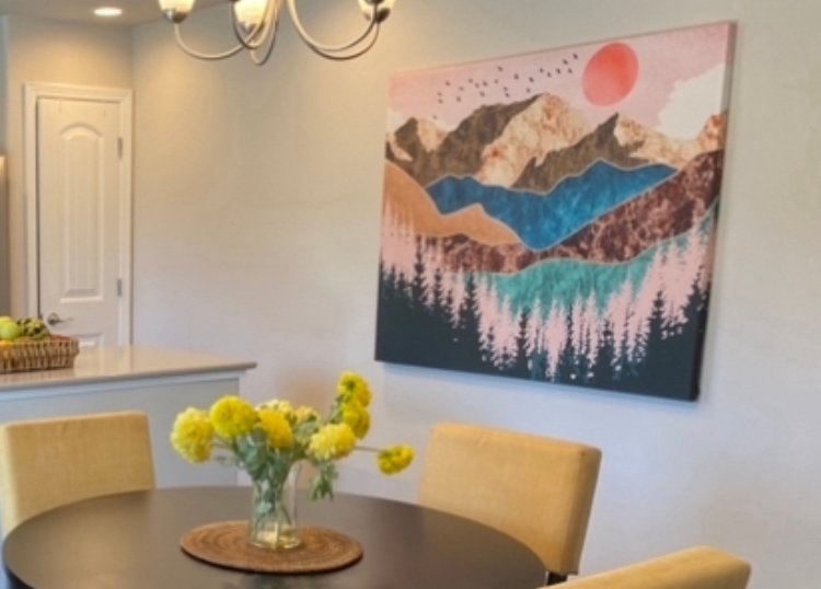 Colorful mountain artwork above a round dining table with yellow flowers