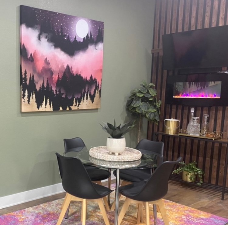 Pink and purple moonlit forest art beside a small dining table and fireplace