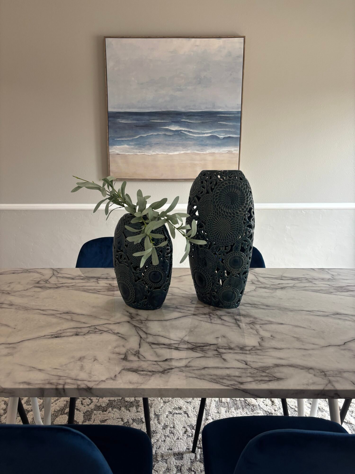 Large framed ocean painting above a dining table with dark decorative vases