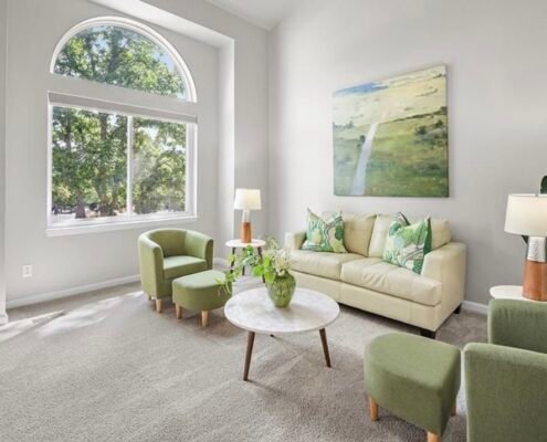 Staged living room with a cream sofa, green chairs and an arched window.