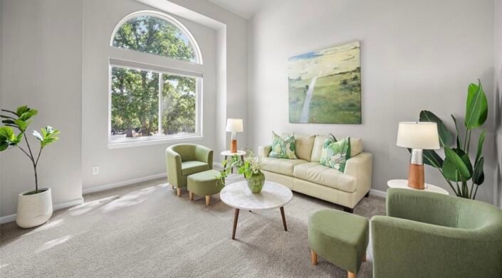Staged living room with a cream sofa, green chairs and an arched window.